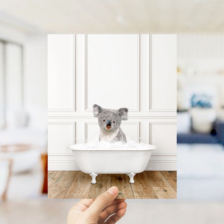 A koala bear sitting in a bathtub filled with water, surrounded by a white interior with a wooden floor.