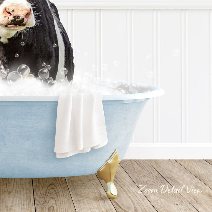 A cow is sitting in a blue bathtub filled with bubbles, with a towel and gold bathtub leg visible.