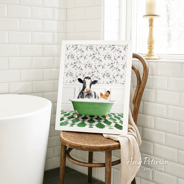 A framed image of a cow and a chicken sitting in a green bathtub, with a floral pattern on the wall behind them.