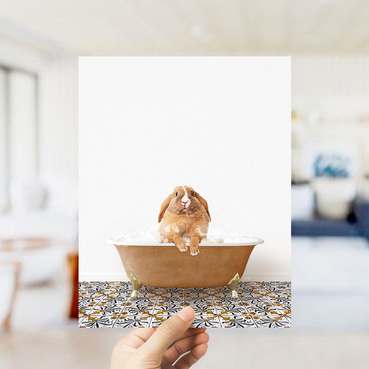 A hand holds up a framed image of a brown rabbit sitting in a bathtub filled with water, surrounded by a patterned tile floor.