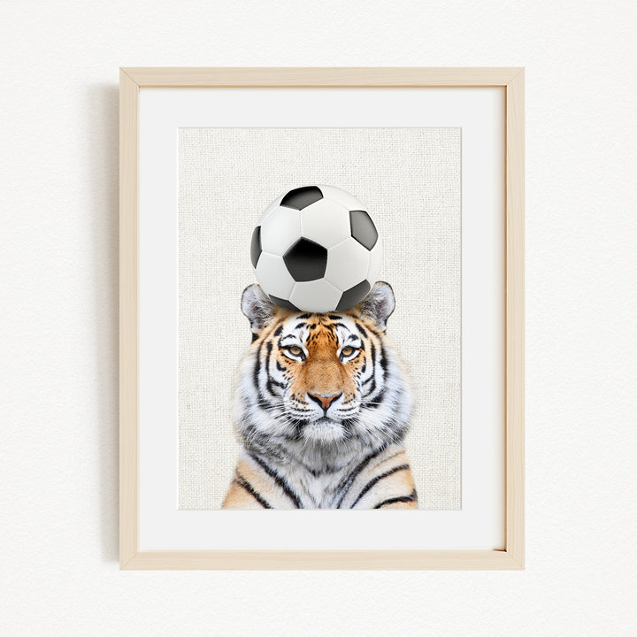 A tiger is sitting on a soccer ball, with the ball placed on its head.