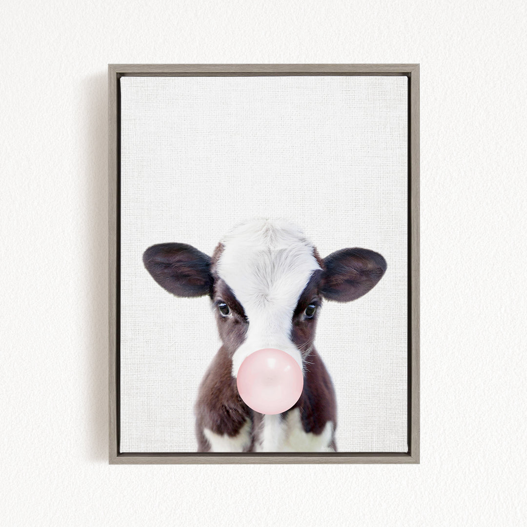 A framed image of a cow blowing a bubble with a pink bubble gum bubble.
