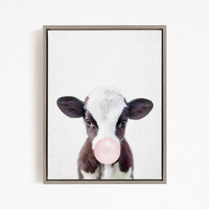 A framed image of a cow blowing a bubble with a pink bubble gum bubble.