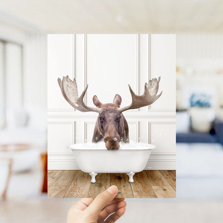 A moose with large antlers is sitting in a white bathtub filled with water, creating a whimsical and humorous scene.