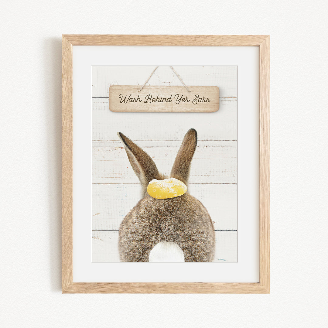 A framed image of a rabbit with a sign that says "Wash Behind Your Ears" hanging above it.