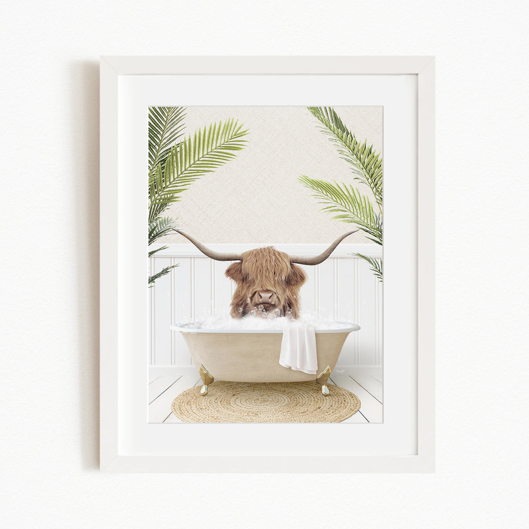 A framed image depicting a Highland cow with long horns sitting in a bathtub filled with bubbles, surrounded by green palm fronds.