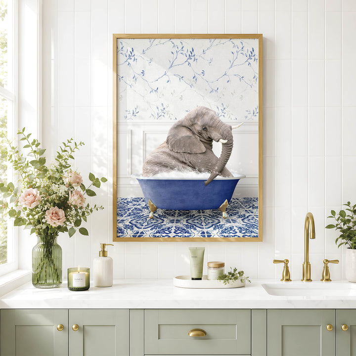 A framed image of a gray elephant sitting in a blue bathtub, surrounded by a floral pattern, is displayed on a white wall above a bathroom counter with various toiletries and a vase of flowers.
