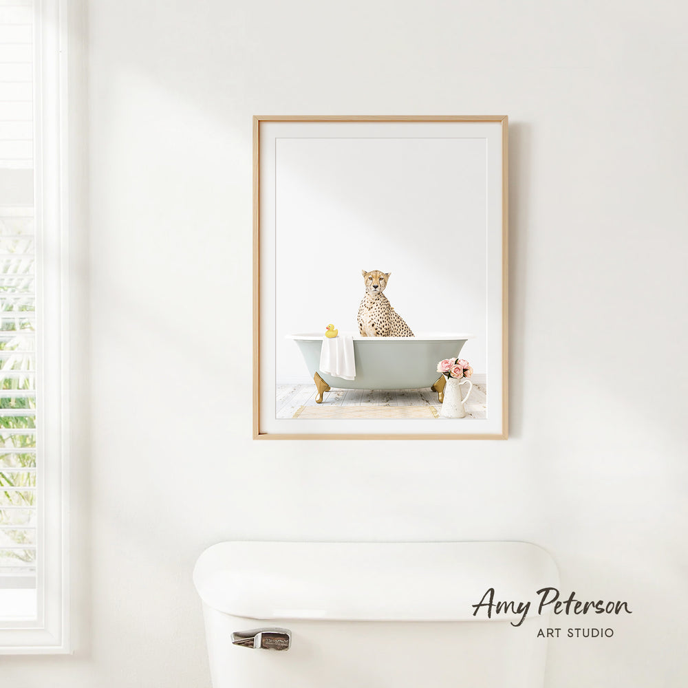 A framed image of a cheetah sitting in a bathtub, with a vase of flowers and a white toilet in the foreground.