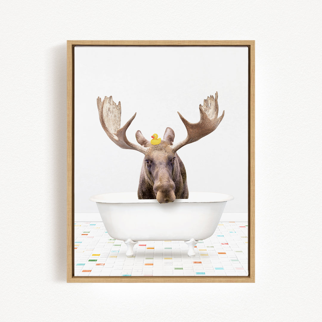 A moose with large antlers is sitting in a white bathtub, with a rubber duck perched on its head.