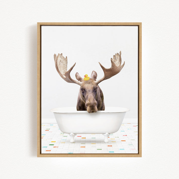 A moose with large antlers is sitting in a white bathtub, with a rubber duck perched on its head.
