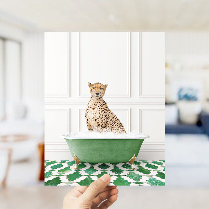A cheetah sitting in a green bathtub filled with bubbles, with a hand holding the image up to the camera.