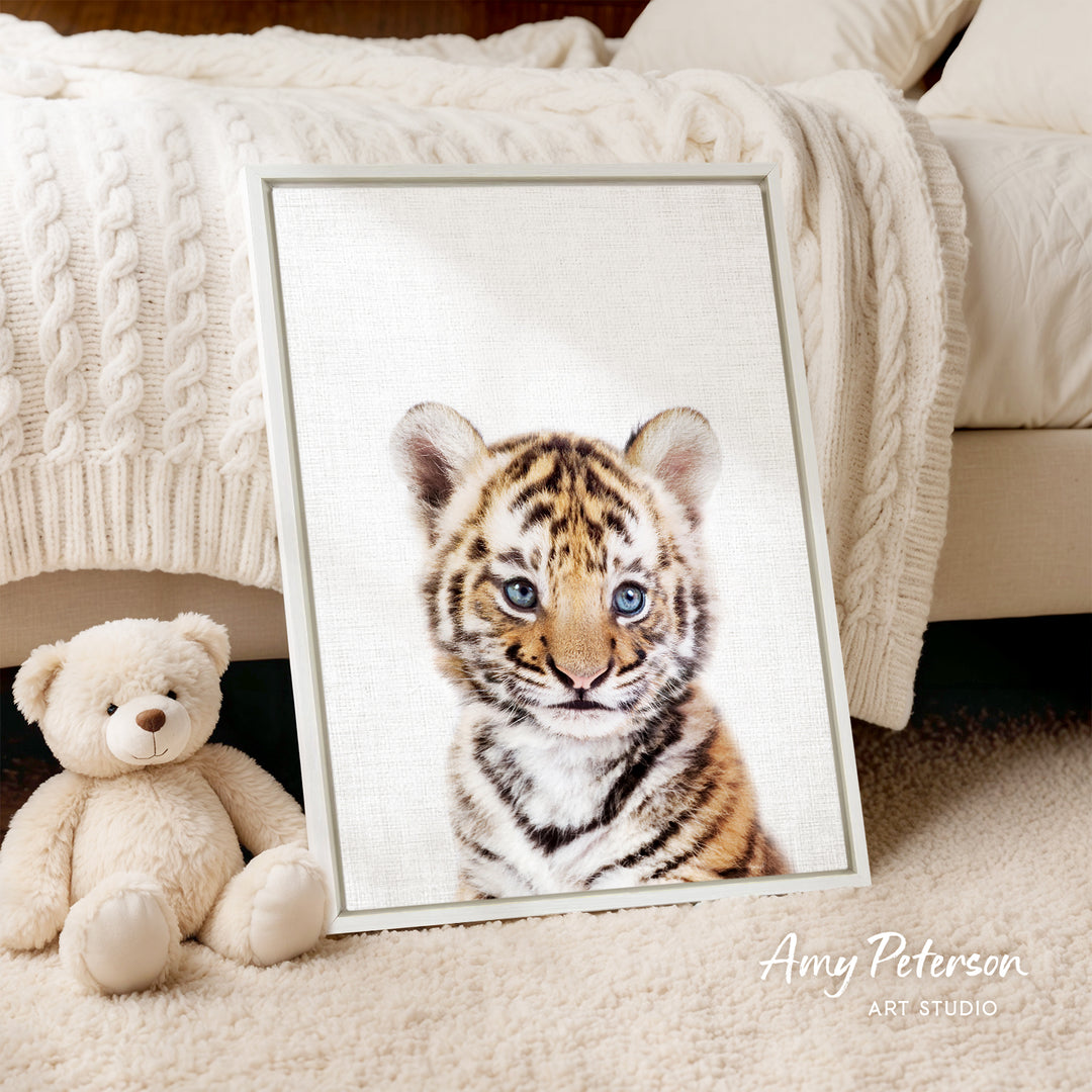 A framed photograph of a tiger cub is displayed on a bed, accompanied by a teddy bear.