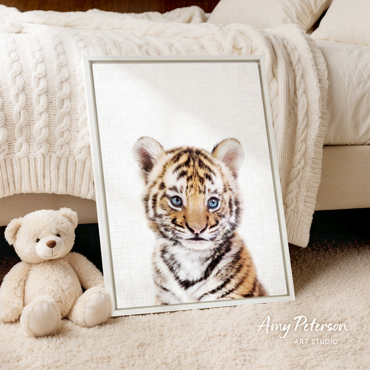 A framed photograph of a tiger cub is displayed on a bed, accompanied by a teddy bear.