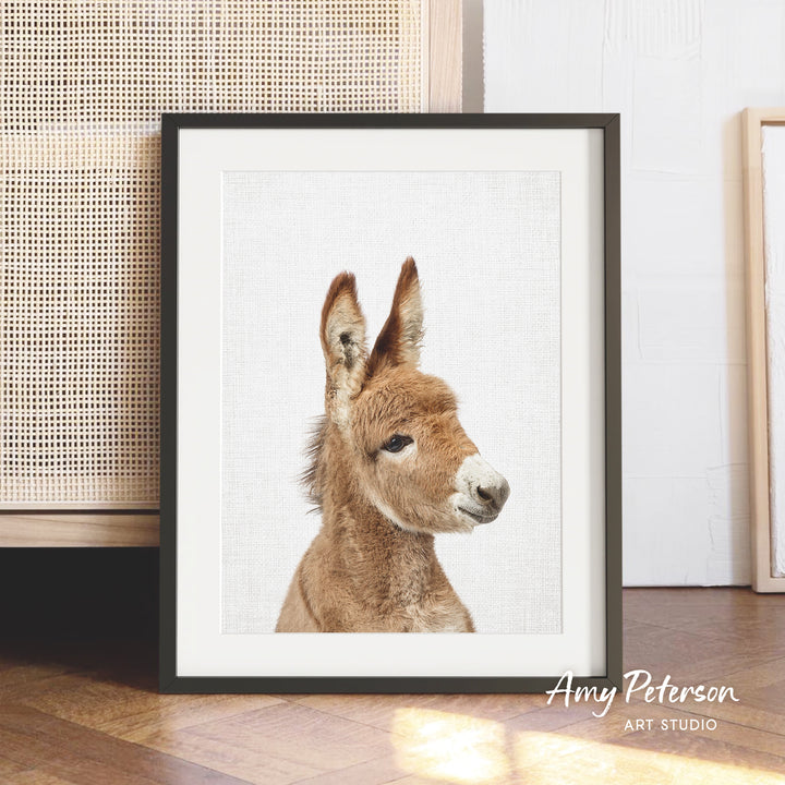 A framed photograph of a donkey's head is displayed on a wooden floor, with a woven basket visible in the background.