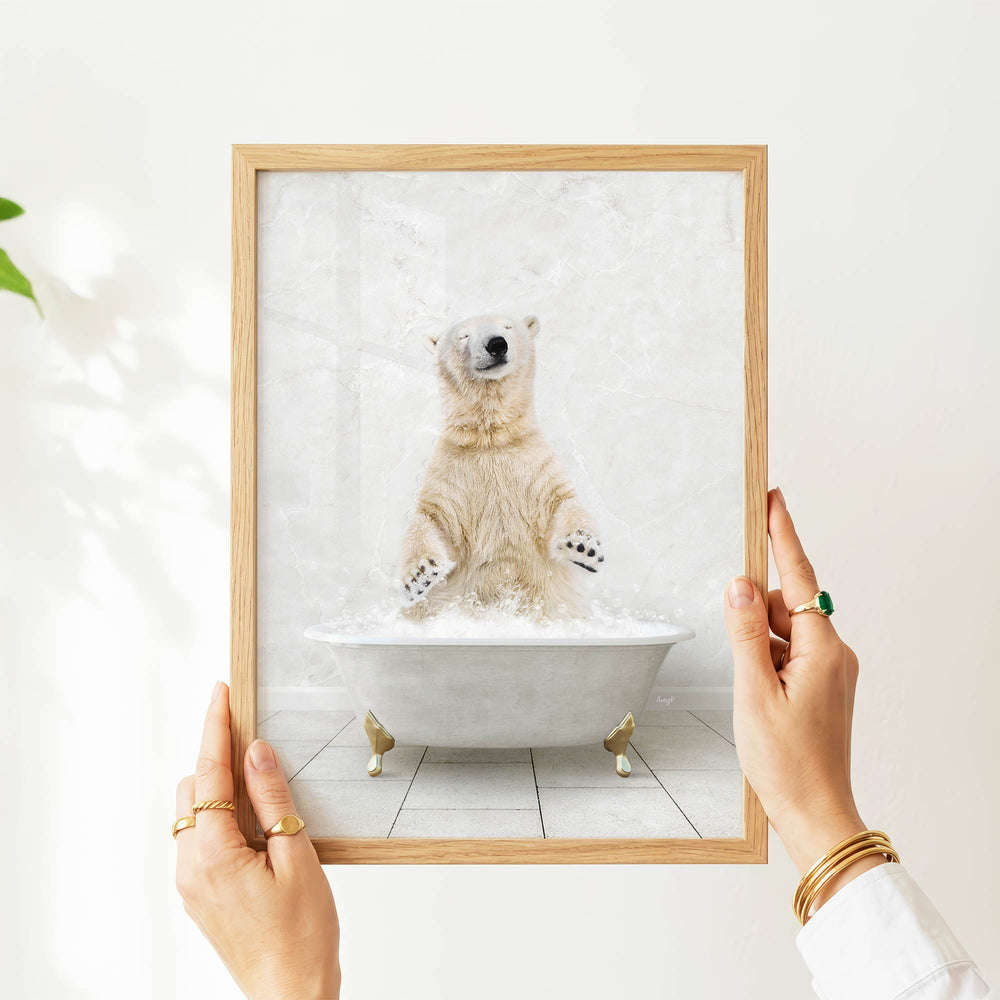 A person's hands are holding a framed picture of a polar bear sitting in a bathtub filled with water.