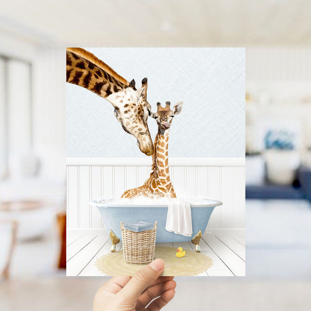 A hand holds up a framed image depicting two giraffes in a bathtub, with one giraffe sitting in the tub and the other standing nearby.