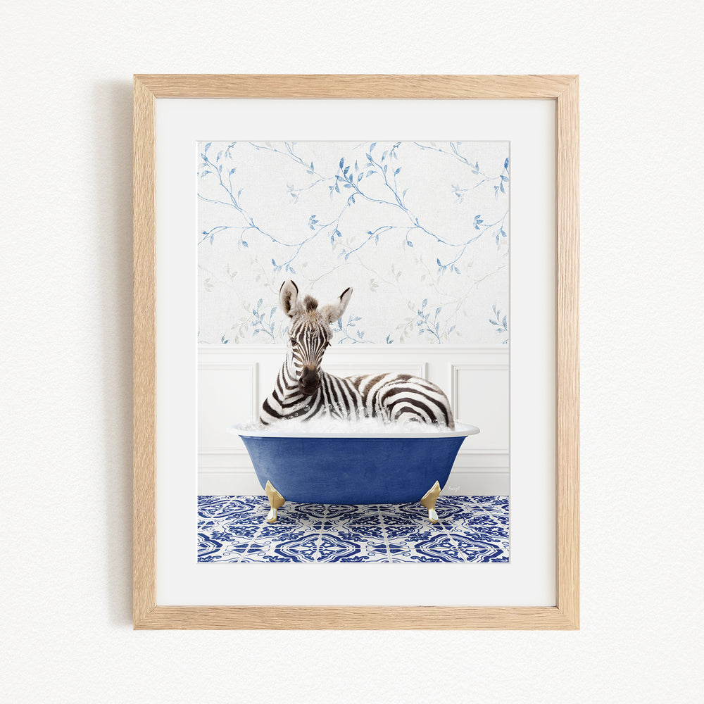 A zebra is sitting in a blue bathtub, surrounded by a blue and white patterned rug and a white wall with blue floral wallpaper.