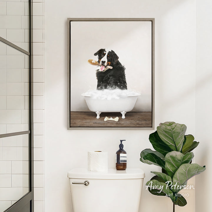 A framed image of a dog sitting in a bathtub, holding a bone, is hanging on a bathroom wall above a toilet.
