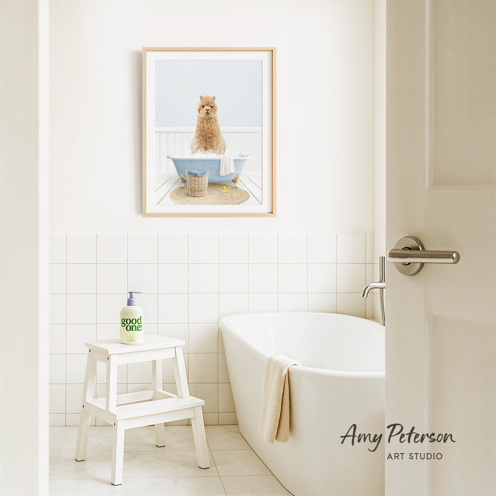 A framed image of a cat sitting in a bathtub is displayed on the wall above a white bathtub in a bathroom.