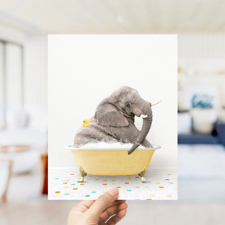 A hand holds up a framed image of a gray elephant sitting in a yellow bathtub, with a yellow rubber duck floating nearby.