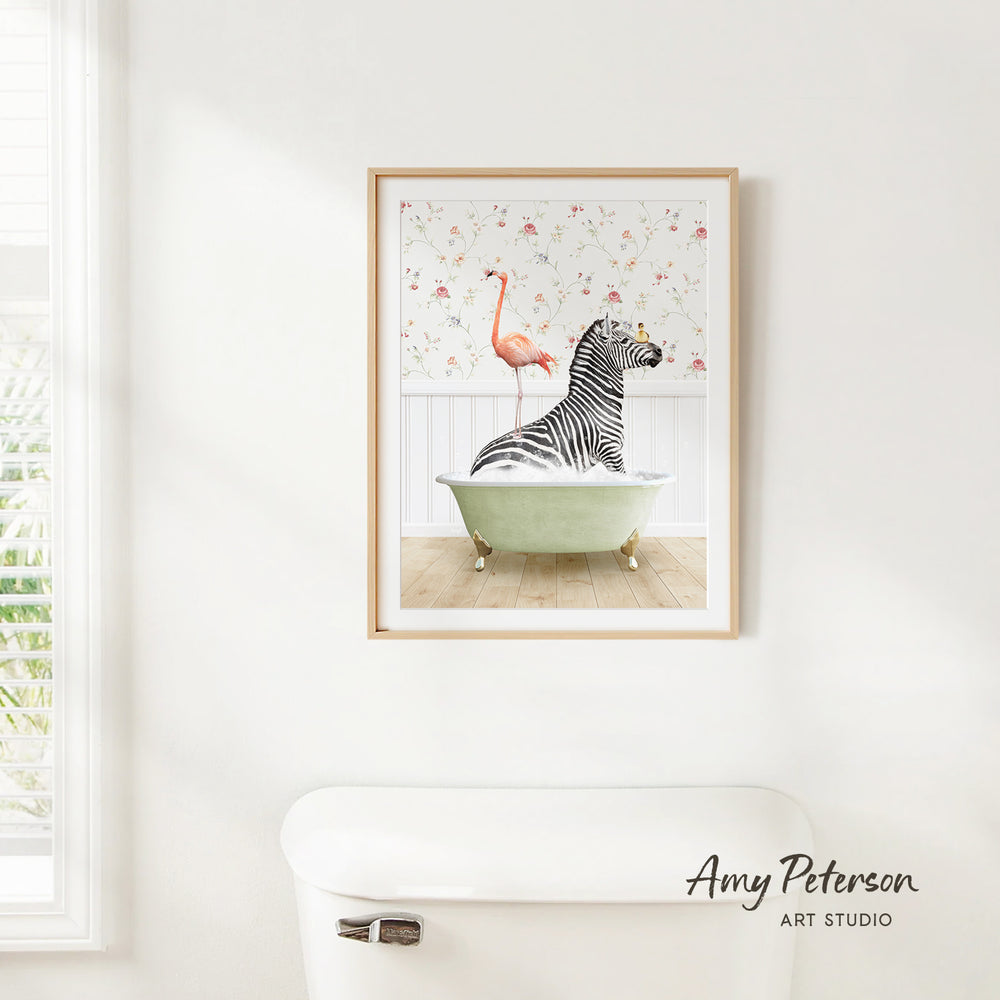A framed print of a zebra sitting in a bathtub, with a pink flamingo standing on the edge of the tub, is hanging on a white wall.