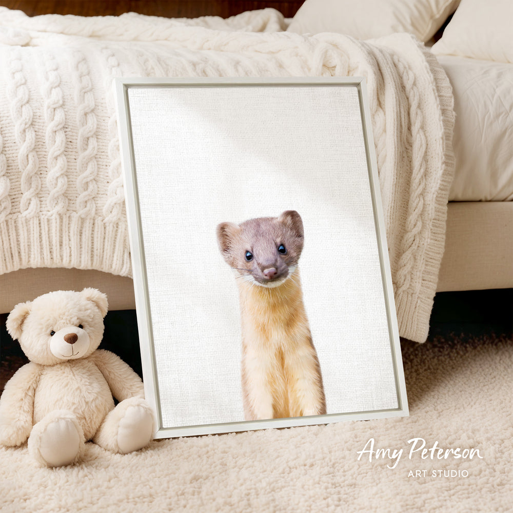 A framed photograph of a curious-looking animal, possibly a small rodent or rodent, is displayed on a white bedspread. Next to the framed photograph is a stuffed teddy bear.