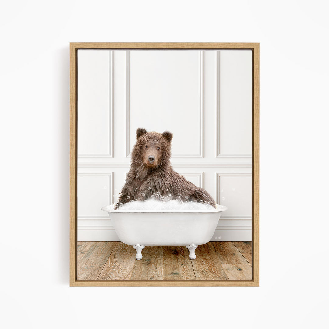 A brown bear sitting in a white bathtub filled with bubbles, looking directly at the camera.