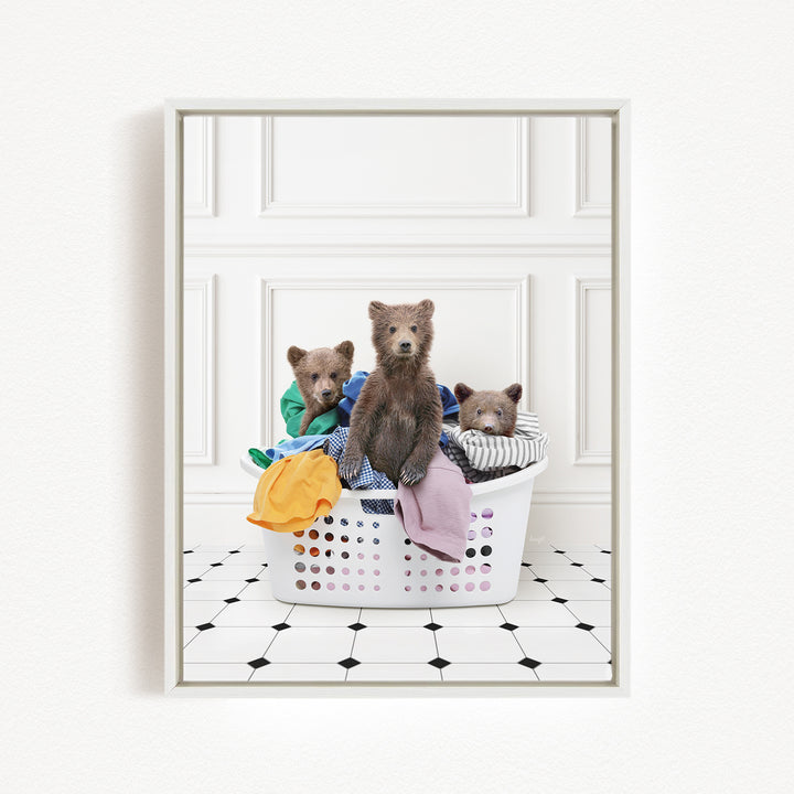 Three adorable brown bears sitting in a white laundry basket filled with clothes.