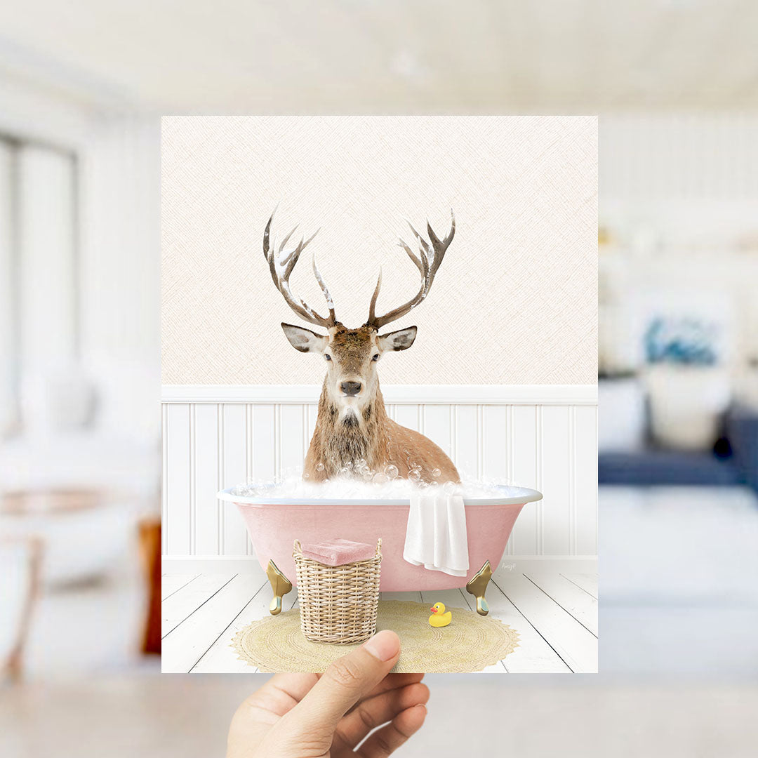 A deer with antlers is sitting in a pink bathtub filled with bubbles, surrounded by a yellow rubber duck and a white towel.