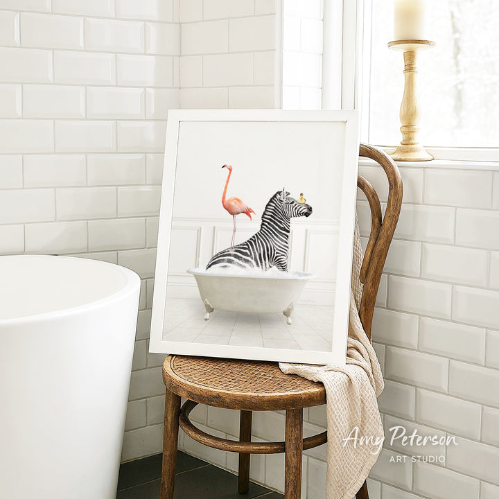 A framed image of a zebra sitting in a bathtub, with a pink flamingo standing on one leg in the background.