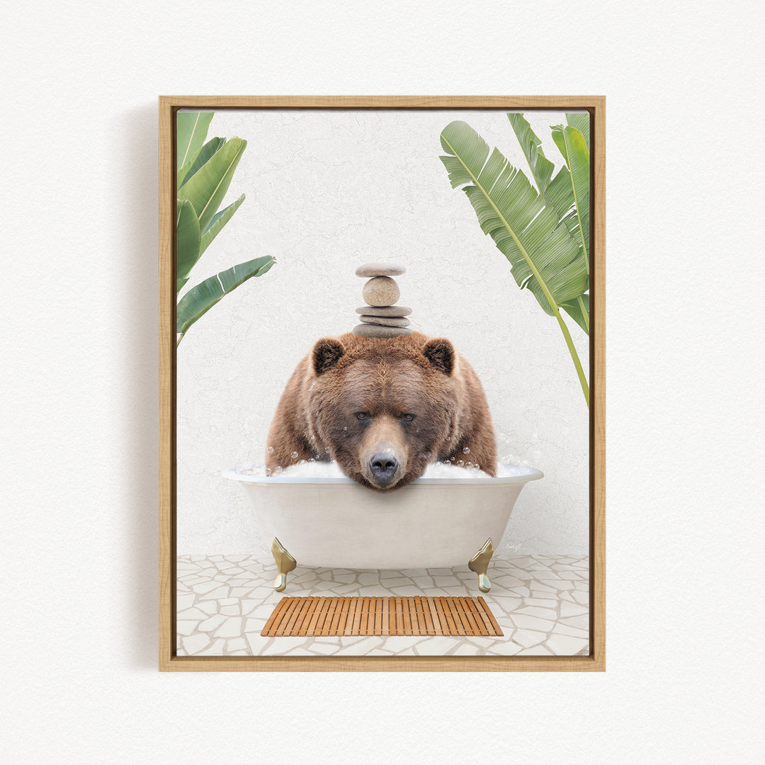 A brown bear is sitting in a white bathtub filled with water, surrounded by green leaves and a wooden mat on the floor.