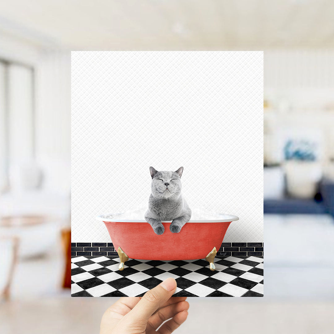 A gray cat sitting in a red bathtub on a black and white checkered floor.