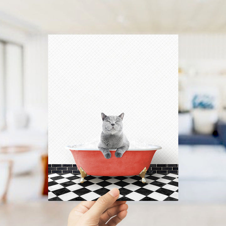 A gray cat sitting in a red bathtub on a black and white checkered floor.