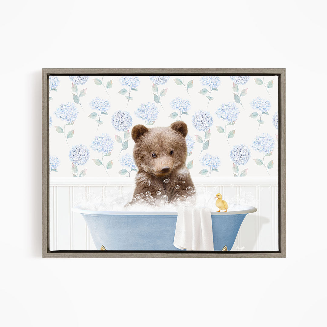 A brown bear sitting in a blue bathtub filled with bubbles, with a yellow duck floating nearby.