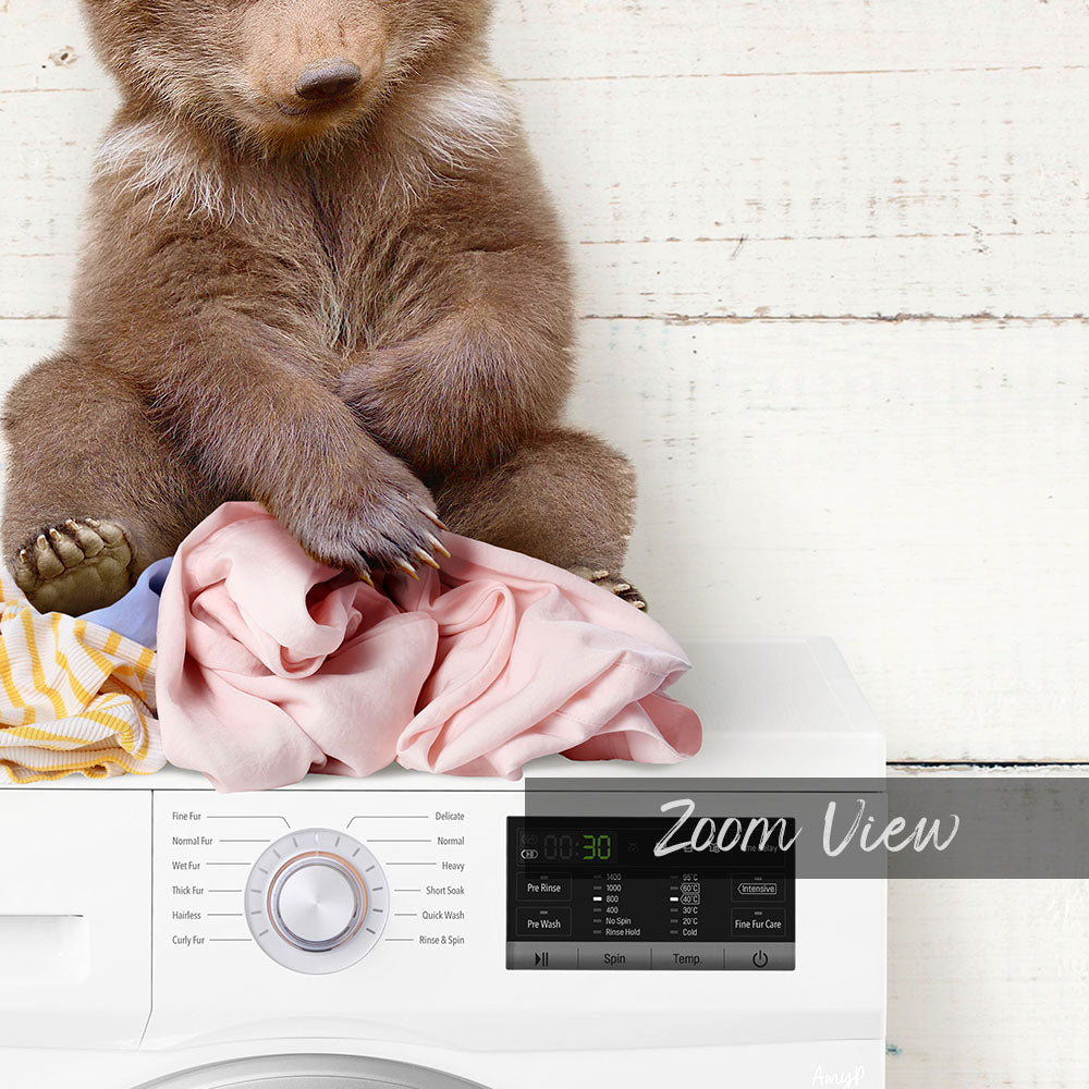 A brown bear sitting on a pile of clothes next to a washing machine.