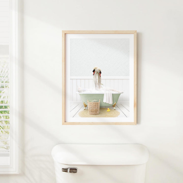 A framed image of a duck sitting in a bathtub, surrounded by a basket of bath toys, is displayed on a white wall above a white toilet.