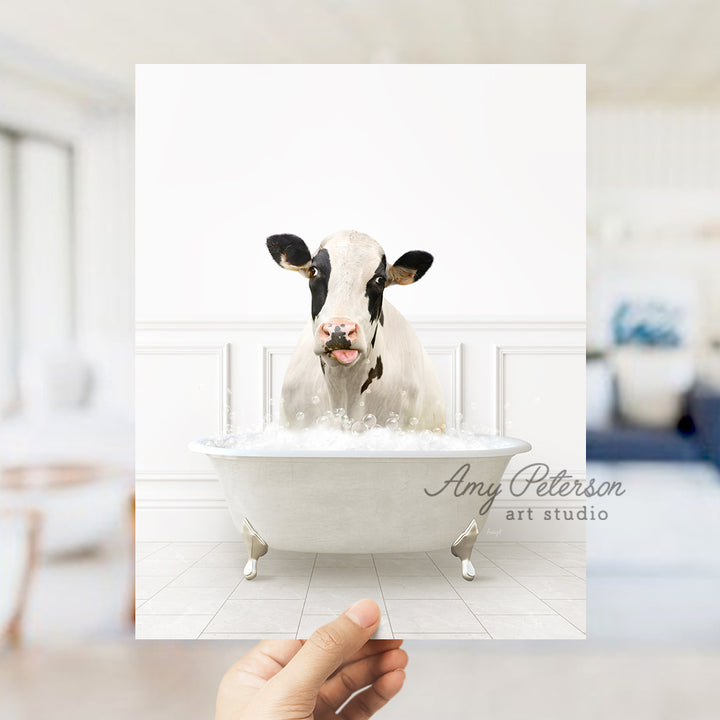 a hand holding up a picture of a cow in a bathtub