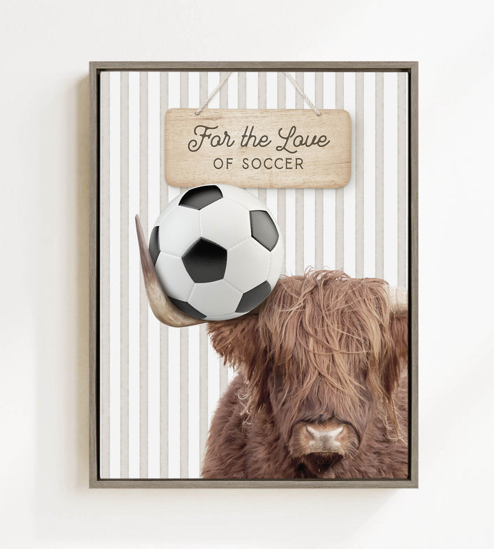 A framed image featuring a brown cow with a soccer ball on its head, with a wooden sign above that says "For the Love of Soccer".