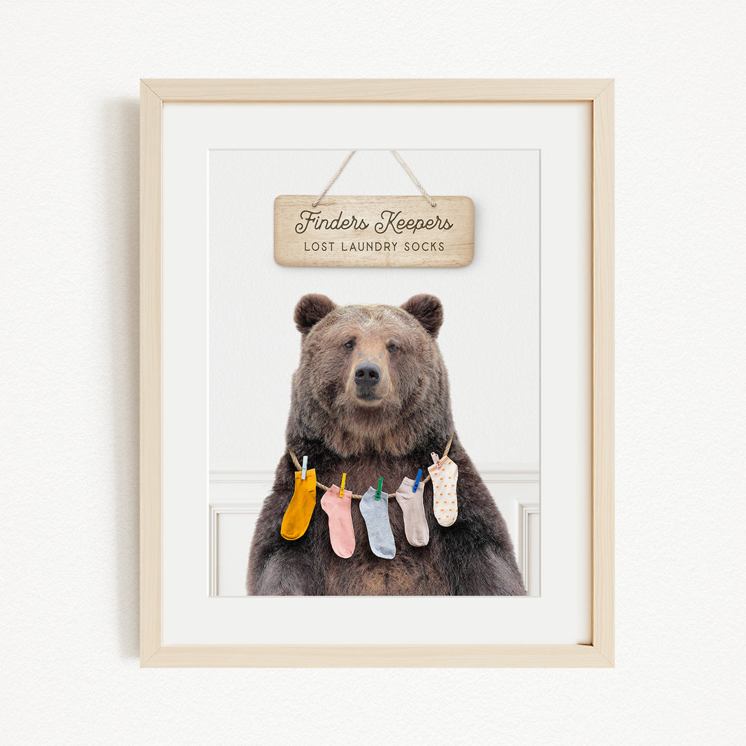 A framed image of a brown bear wearing colorful socks hanging on a clothesline.