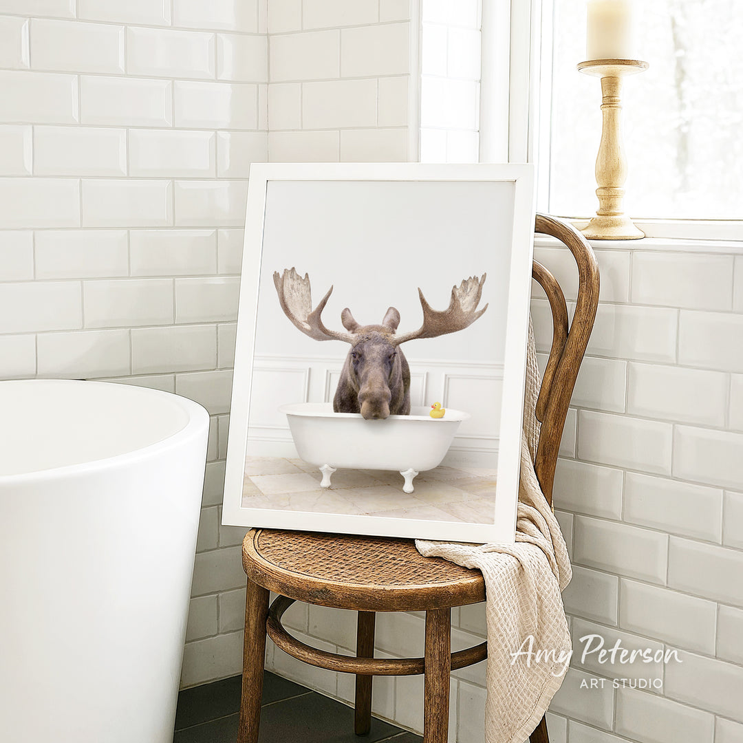 A framed image of a moose sitting in a bathtub, with a yellow rubber duck floating in the water.