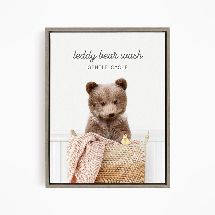 A teddy bear sitting in a woven basket, with a blanket and a small toy duck nearby.