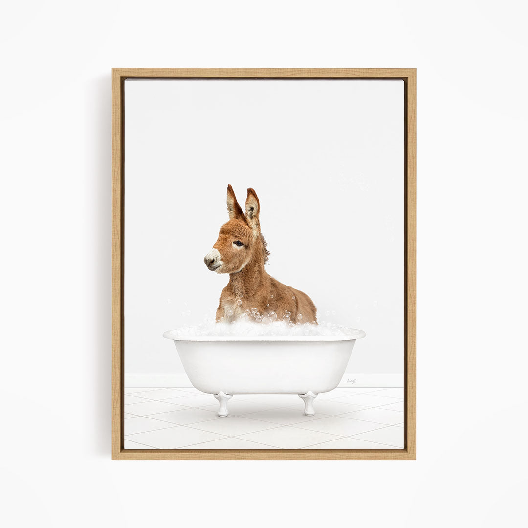 A donkey is sitting in a white bathtub filled with bubbles, looking directly at the camera.
