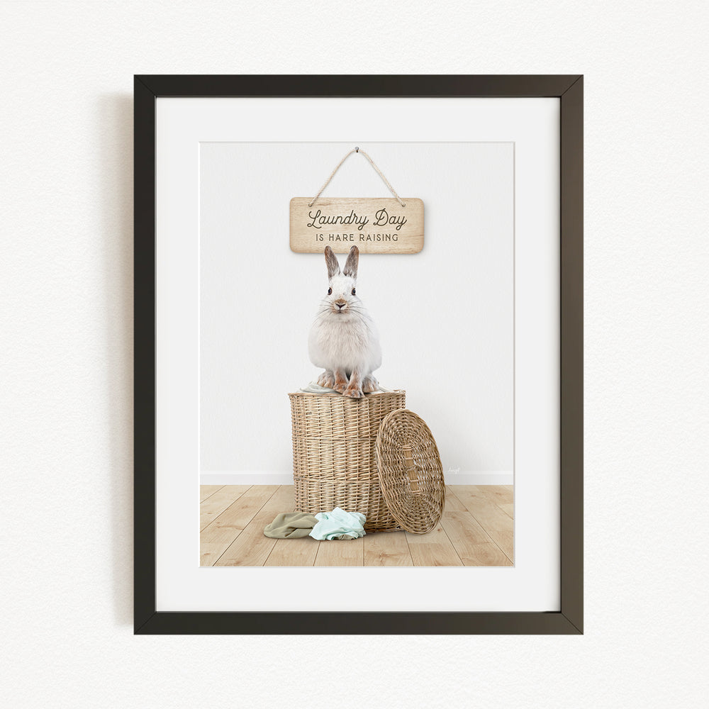 A white rabbit sits atop a wicker basket, with a wooden sign above that reads "Laundry Day is hard washing".