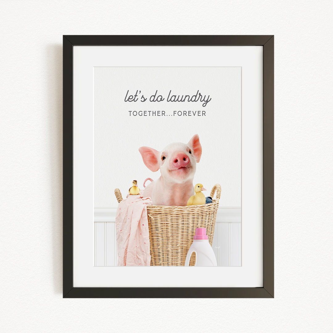 A framed image of a pig sitting in a wicker basket filled with rubber ducks, accompanied by the text "let's do laundry together forever".
