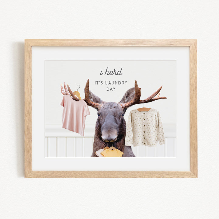 A framed image depicting a moose holding clothes, with the text "It's laundry day" above it.