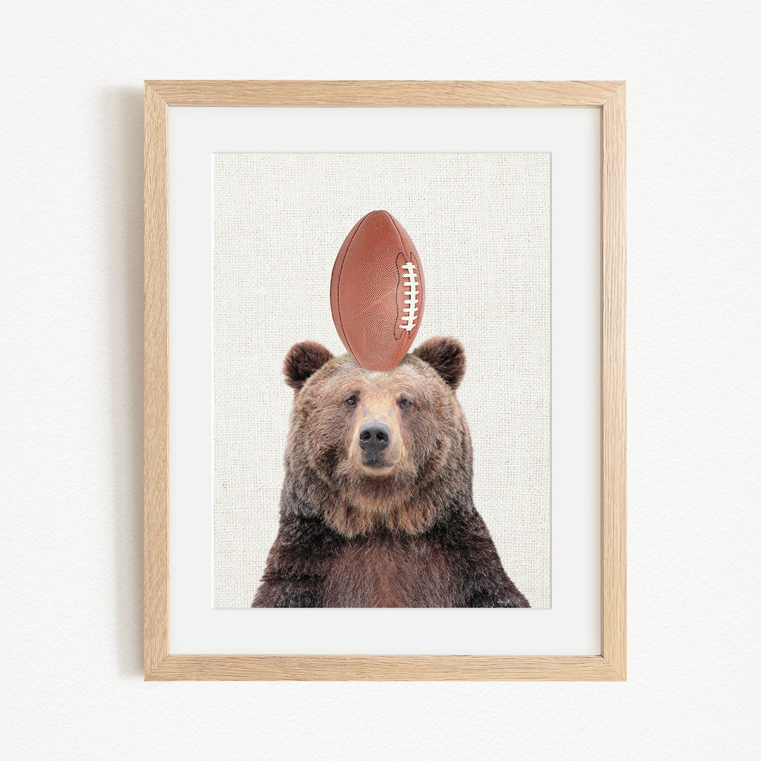 A framed image of a brown bear with a football on its head.