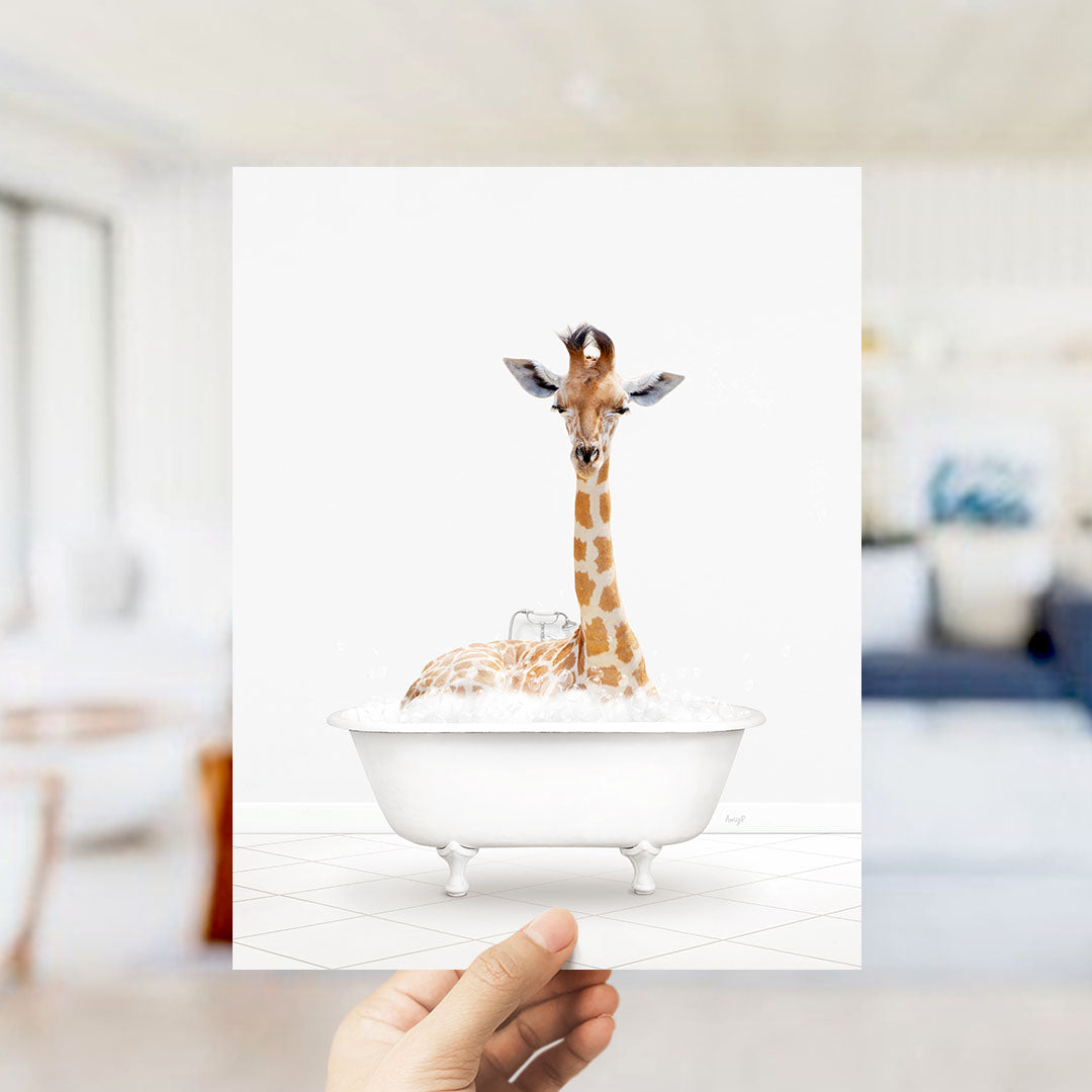 A giraffe sitting in a white bathtub filled with water, with a person's hand holding the image up to the camera.