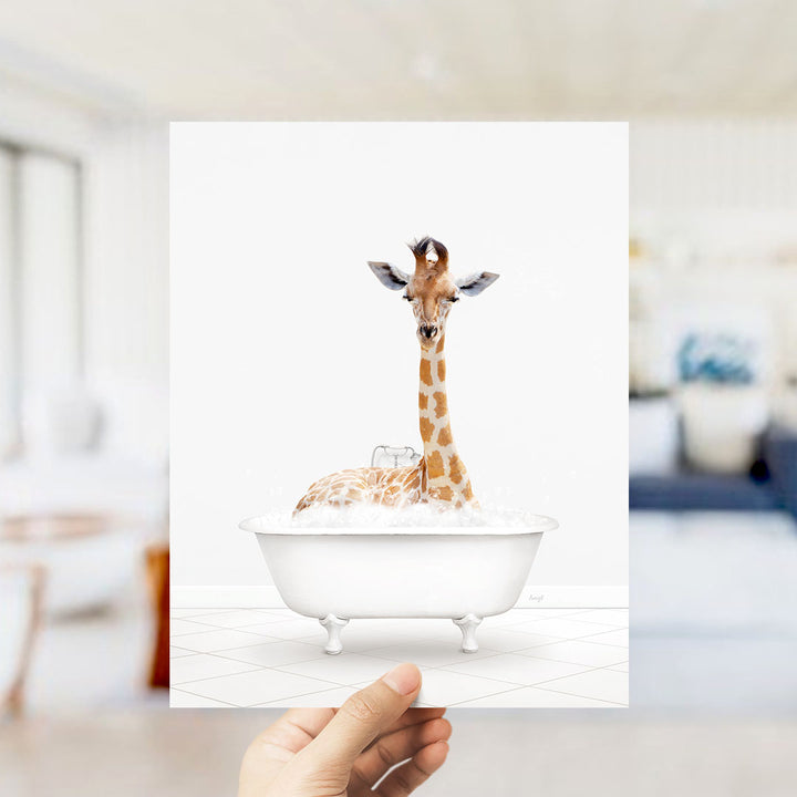 A giraffe sitting in a white bathtub filled with water, with a person's hand holding the image up to the camera.