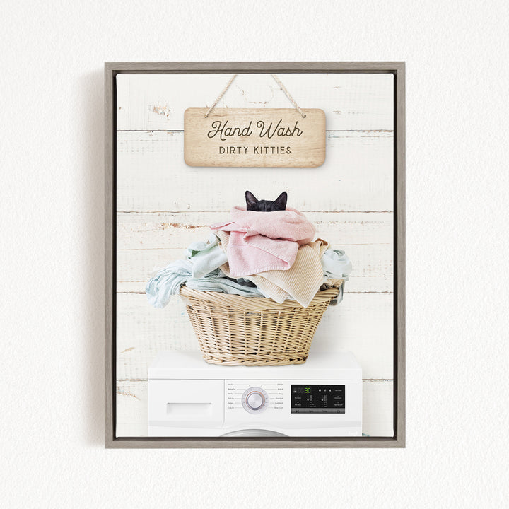 A framed image depicting a cat sitting in a basket filled with laundry, with a sign above that reads "Hand Wash Dirty Kitties".