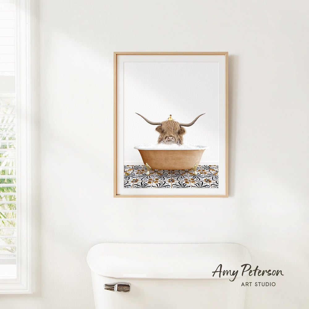 A framed print of a Highland cow sitting in a bathtub is hanging on a white wall.